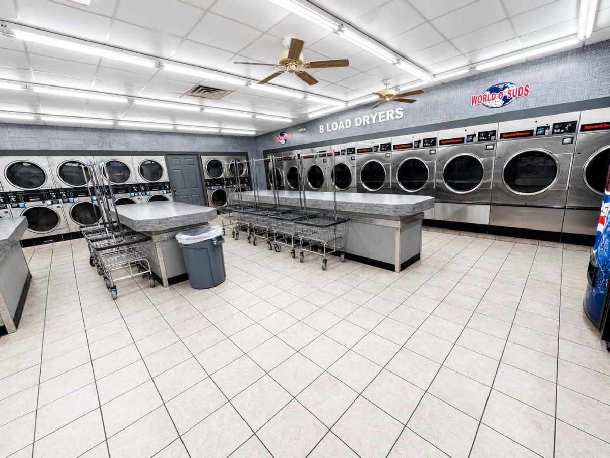 World O' Suds Coin Laundry, 430 E Main St Apopka FL — vista amplia del cuarto de secadoras comerciales de 8 cargas con mesas de doblado de marca y mural de pared de World O' Suds