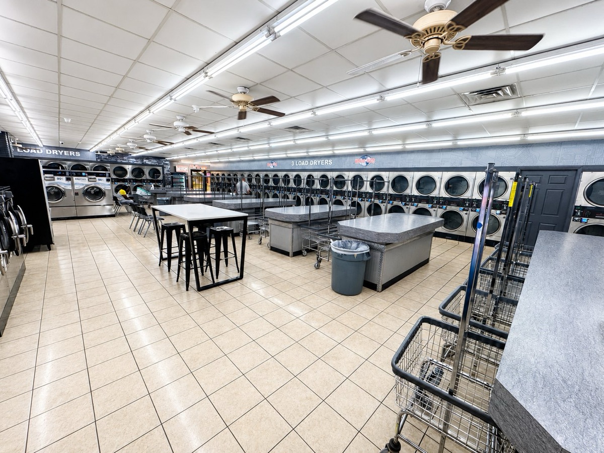World O' Suds Coin Laundry, 430 E Main St Apopka FL — vista amplia del piso principal de la lavandería con hileras de secadoras a ambos lados y mesas de doblado en el pasillo central